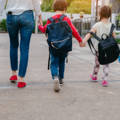 rear view of a mother and 2 young children with rucksacks on their backs walking.