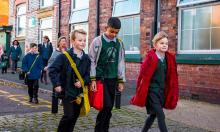 School children walking along a street with houses in the background