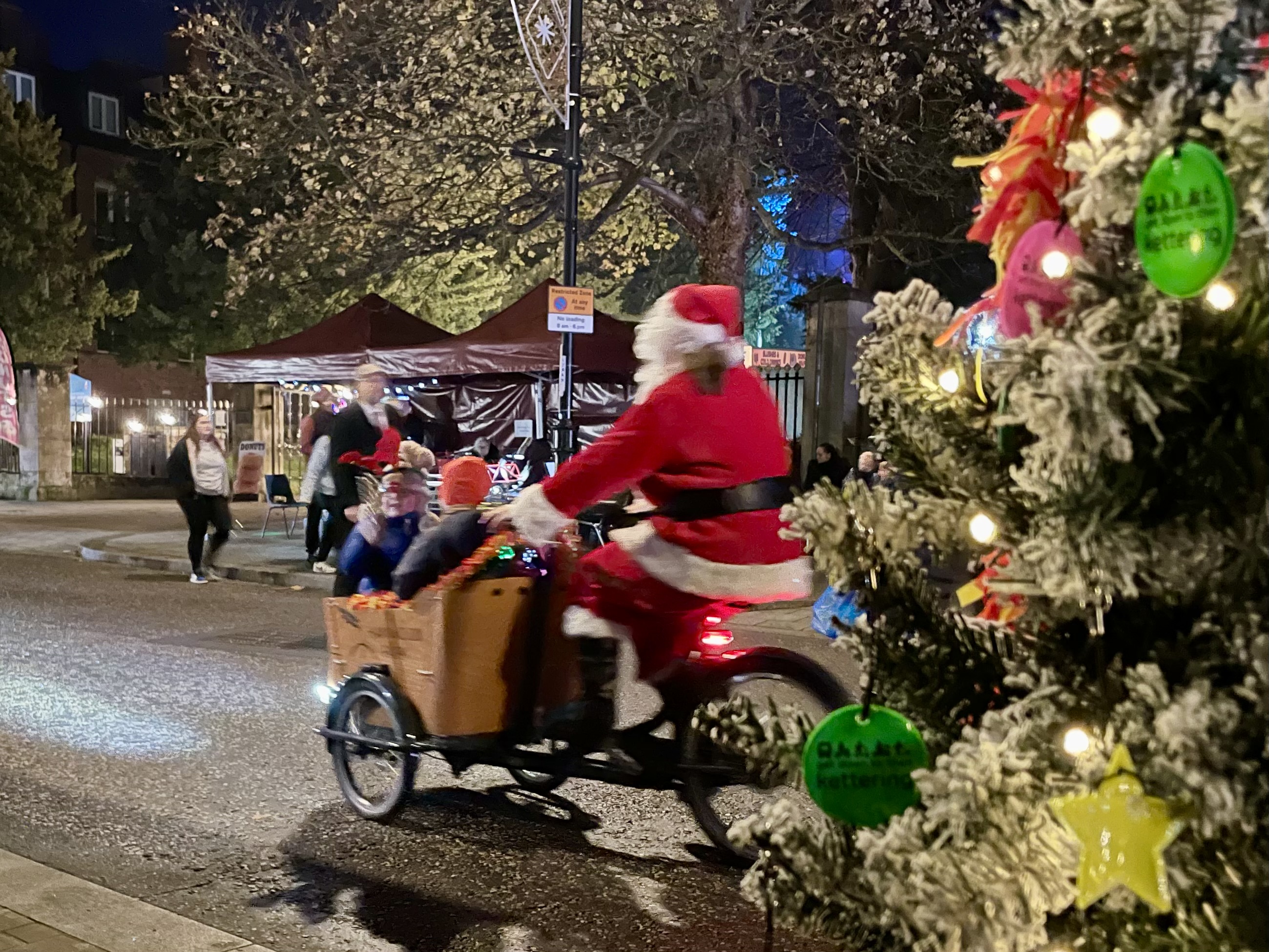 Santa cycling past the brightwayz Christmas tree.
